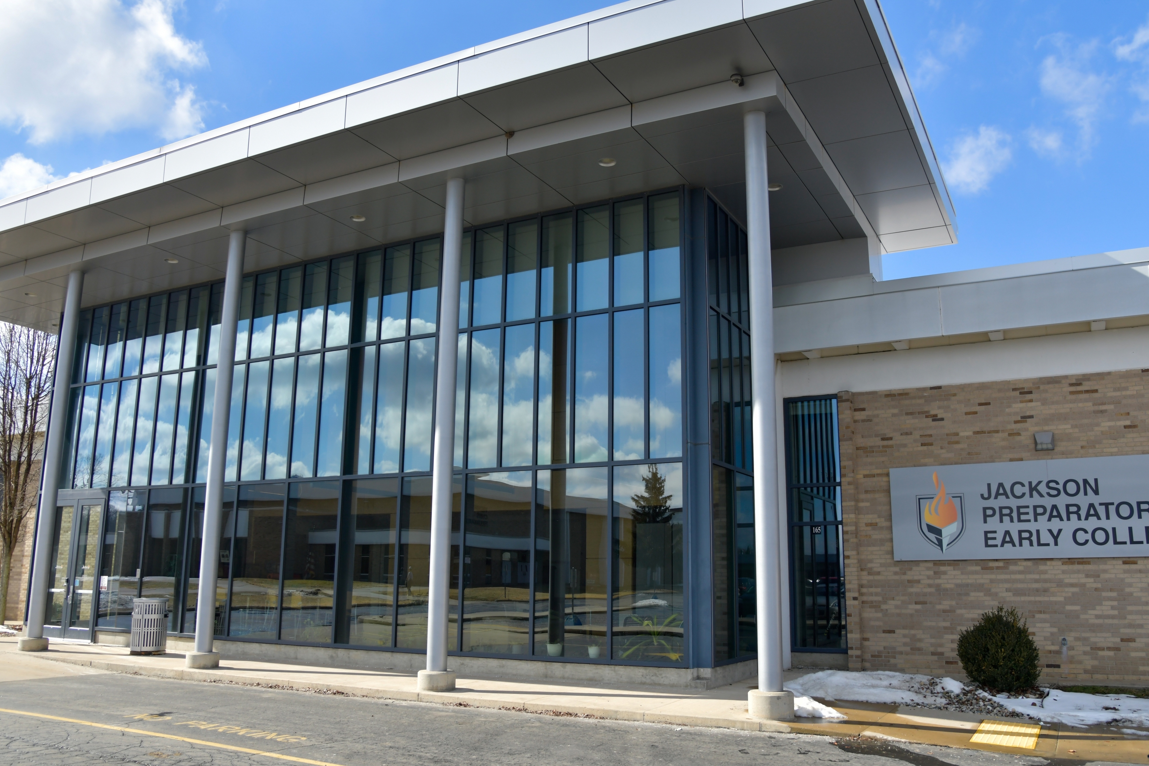 The front of the Jackson Preparatory Early College Building in Jackson, MI. The building has tall columns and glass windows that reflect other JPEC buildings. 