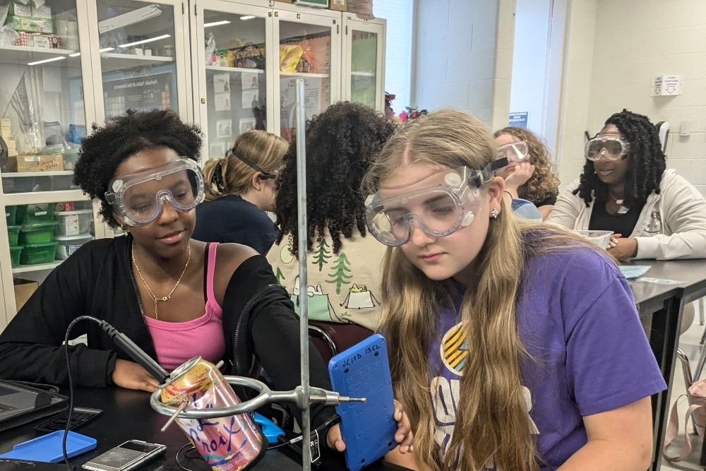 Two JPEC students are wearing goggles and working with lab equipment in a lab classroom.