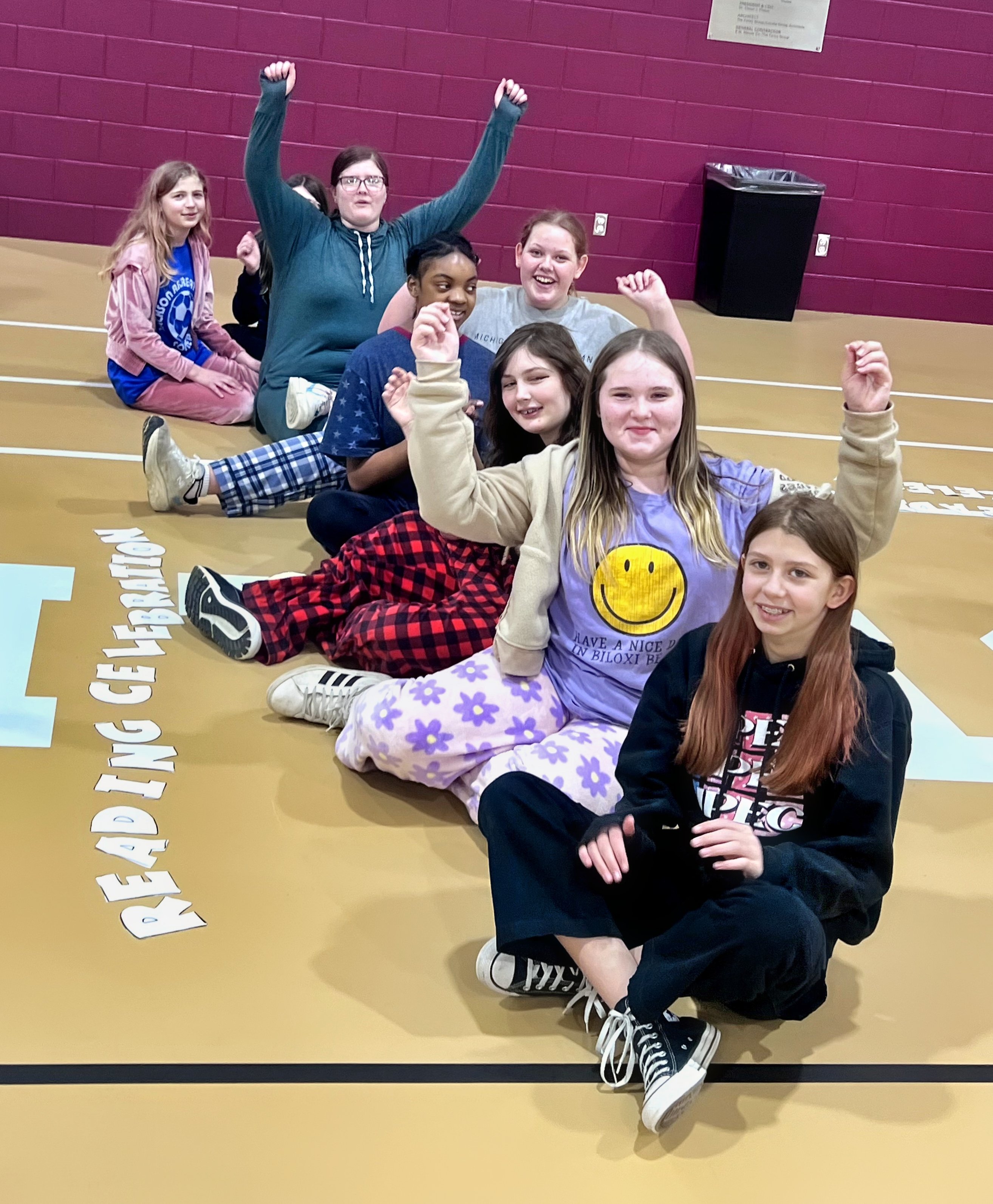 a row of Jackson Preparatory & Early College students sit on the gym floor and raise their hands in a cheer.